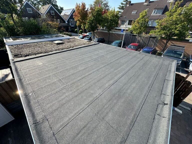 Plat dak met grind naast huizen en bomen.