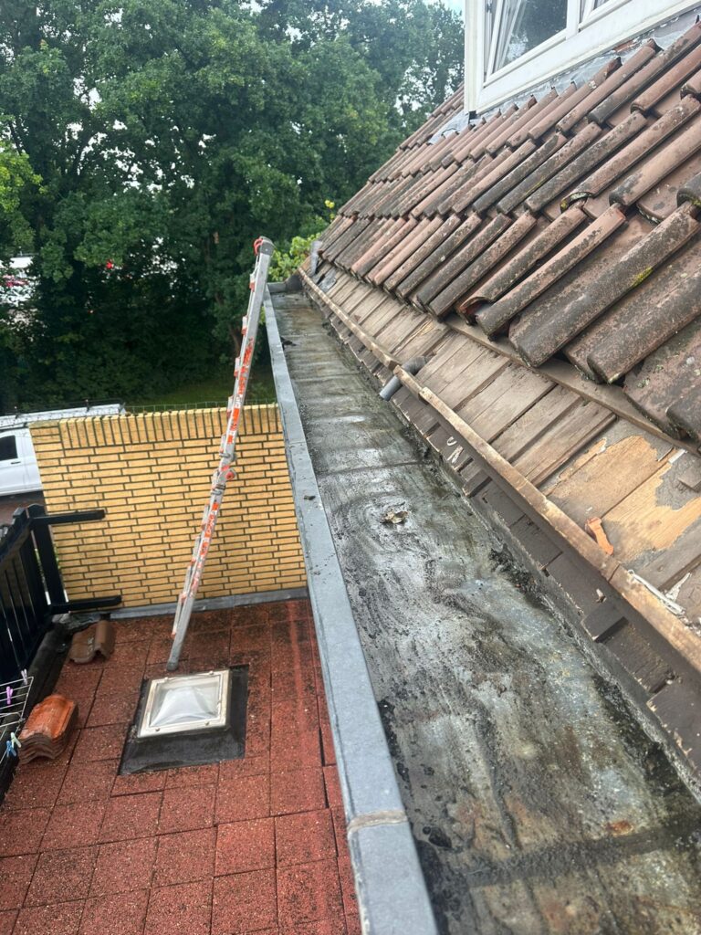 Verstopte dakgoot naast betonnen dakterras.