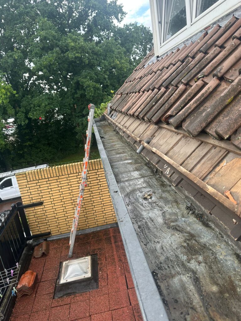 Verstopte dakgoot met ladder en dakpannen.