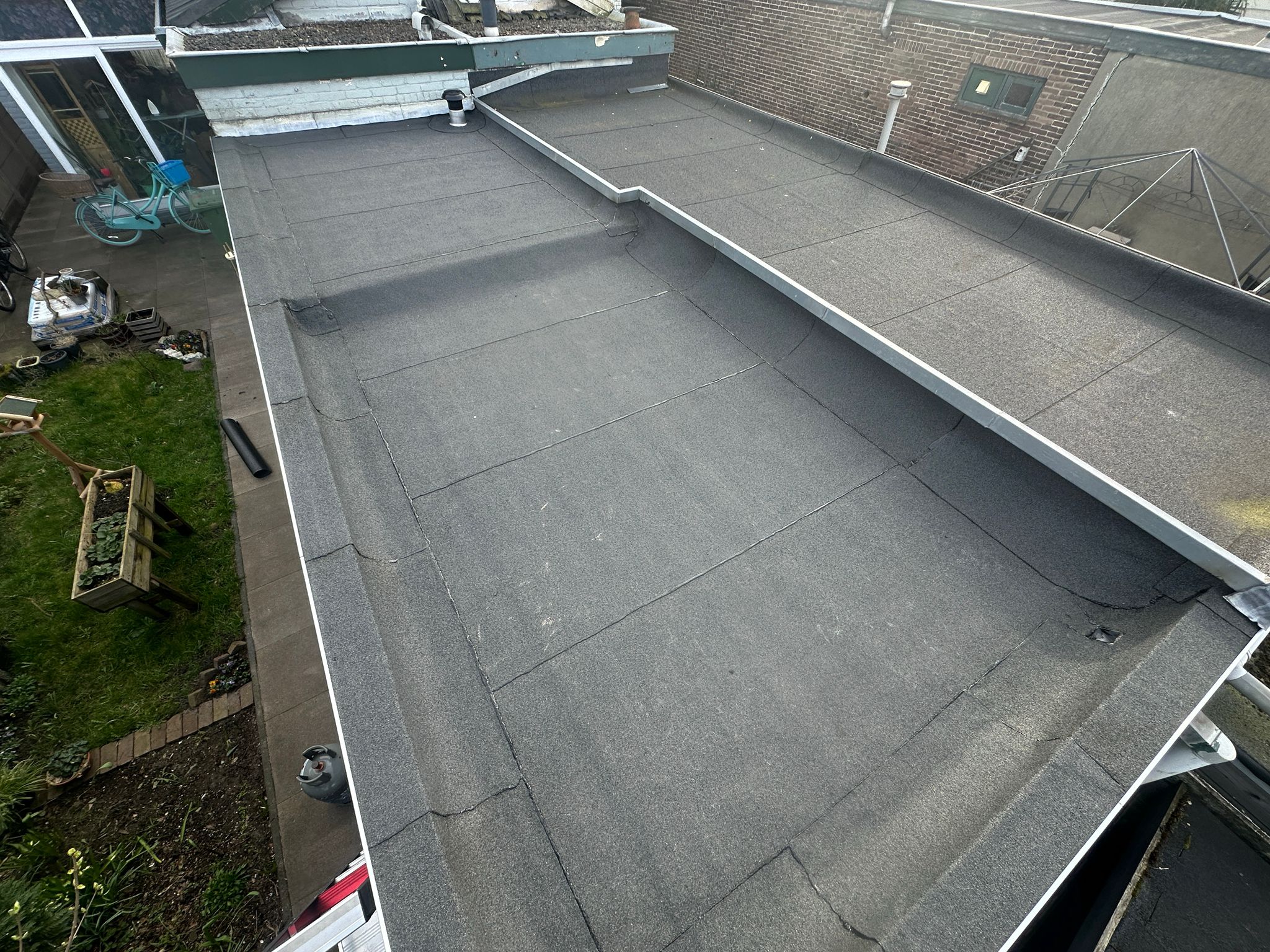 Plat dak van bitumen met omliggende tuin en fietsen.