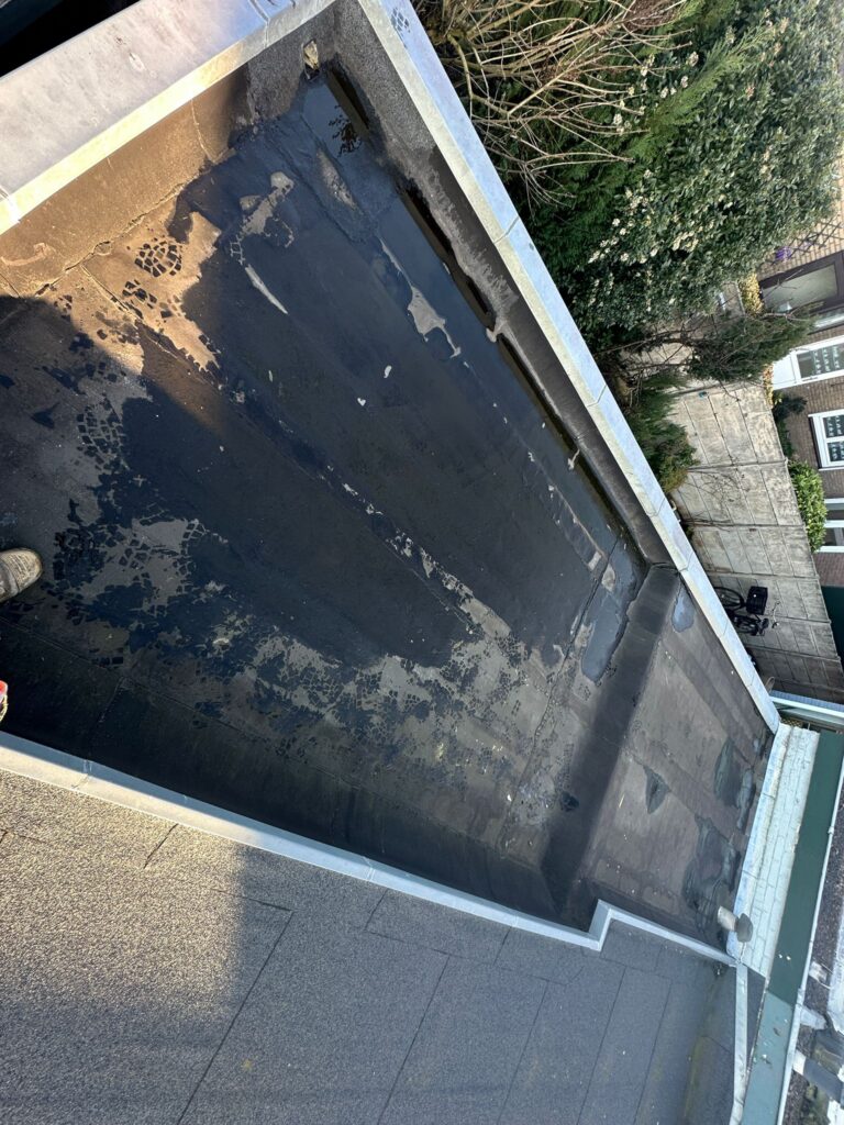 Plat dak met beschadigde asfaltbedekking bij gebouwrand.